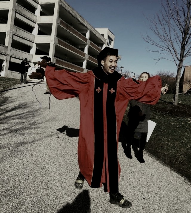 Dr. Hieu in doctoral robes, arms spread, on graduation day